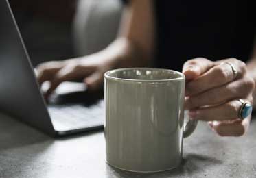 picture of a women sitting on a laptop with a cup of coffee in front of her and a turquoise ring on using facebook for your business 